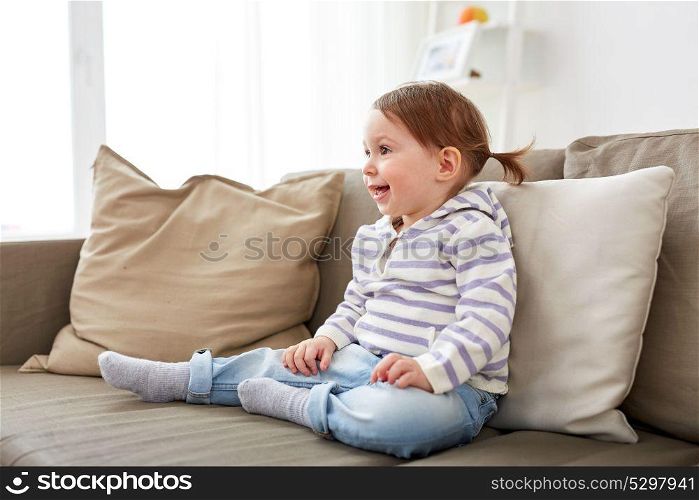 childhood and people concept - happy smiling baby girl sitting on sofa at home. happy smiling baby girl sitting on sofa at home