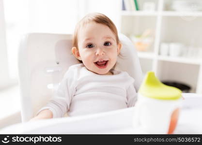 childhood and people concept - happy smiling little baby sitting in highchair at home. happy smiling baby sitting in highchair at home