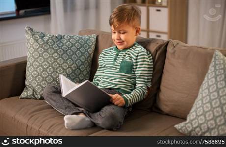 childhood and people concept - happy smiling little boy reading book at home. happy smiling little boy reading book at home