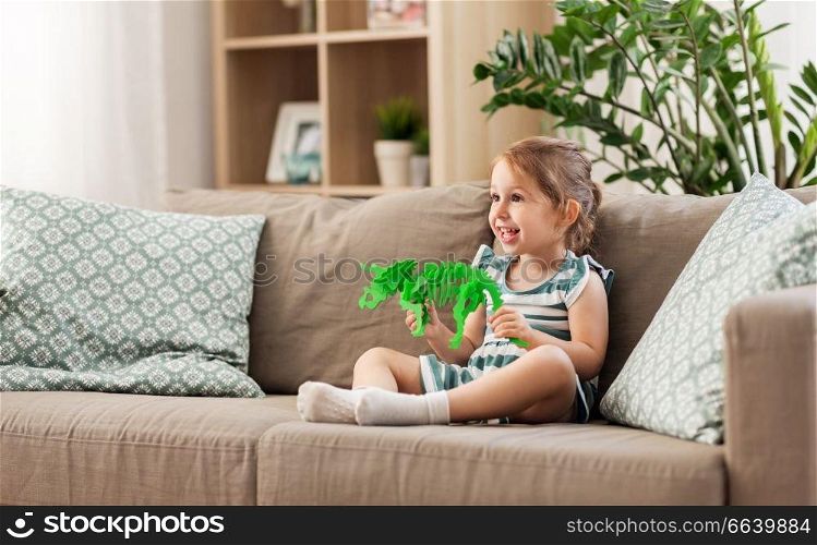 childhood and people concept - happy three years old baby girl playing with toy dinosaur skeleton at home. happy baby girl playing with toy dinosaur at home