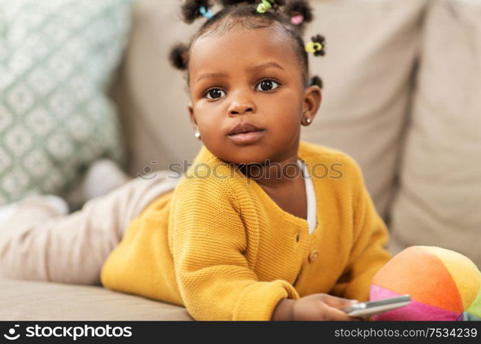 childhood and people concept - little african american baby girl playing with ball and smartphone at home. african american baby girl with smartphone at home
