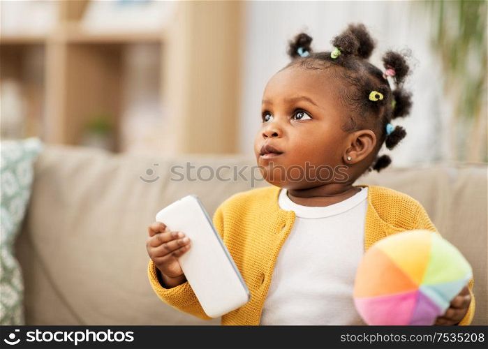 childhood and people concept - little african american baby girl playing with ball and smartphone at home. african american baby girl with smartphone at home