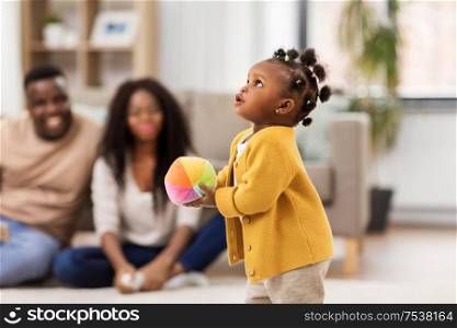 childhood and people concept - little african american baby girl playing with ball and parents at home. african american baby girl with ball at home