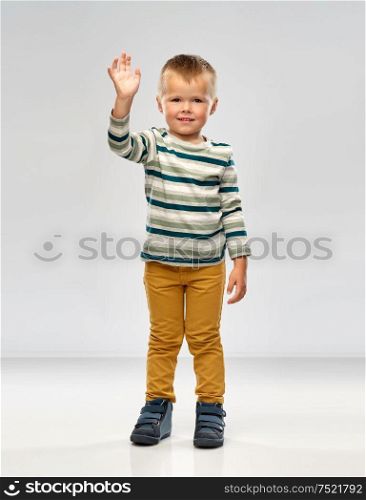 childhood and people concept - little boy in striped shirt waving hand over grey background. little boy in striped shirt waving hand