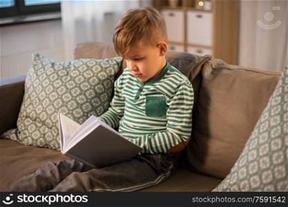 childhood and people concept - little boy sitting on sofa and reading book at home. little boy reading book at home