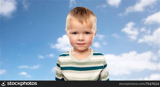 childhood and people concept - portrait of little boy in striped shirt over blue sky and clouds background. little boy in striped shirt over blue sky