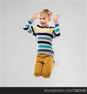 childhood and people concept - portrait of nice little boy in striped pullover jumping and having fun over grey background. happy little boy jumping and having fun