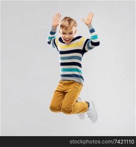 childhood and people concept - portrait of nice little boy in striped pullover jumping and having fun over grey background. happy little boy jumping and having fun