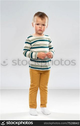 childhood and people concept - portrait of sad little boy in striped shirt over grey background. portrait of sad little boy in striped shirt