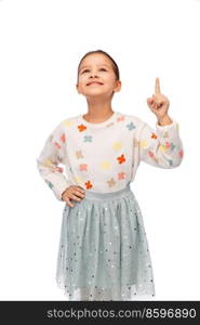 childhood and people concept - portrait of smiling little girl pointing finger and looking up over white background. happy girl pointing finger up