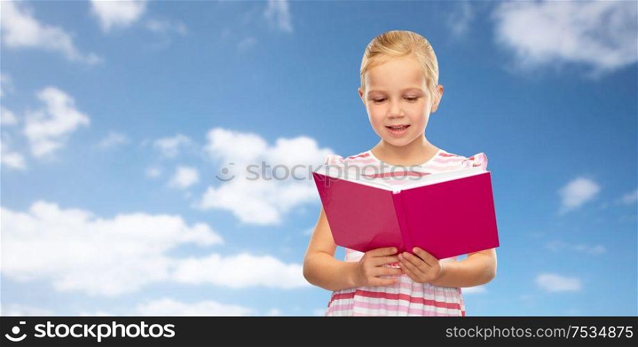childhood and people concept - smiling little girl reading book over blue sky and clouds background. little girl reading book over sky background