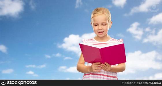 childhood and people concept - smiling little girl reading book over blue sky and clouds background. smiling little girl reading book