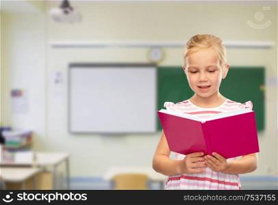 childhood and people concept - smiling little girl reading book over classroom background. smiling little girl reading book