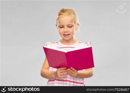 childhood and people concept - smiling little girl reading book over grey background. smiling little girl reading book