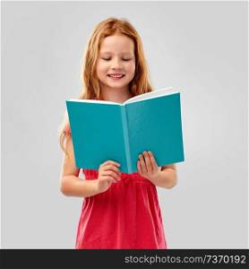 childhood and people concept - smiling red haired girl reading book over grey background. smiling red haired girl reading book