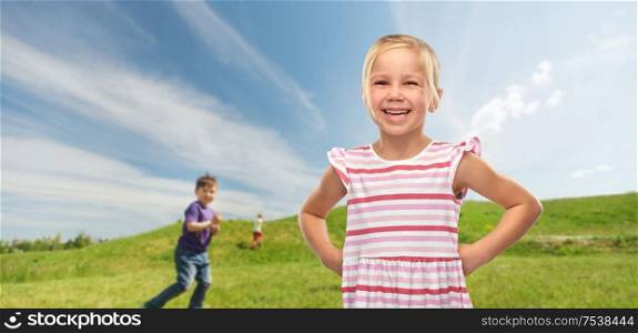 childhood and summer concept - smiling little girl in striped dress over blue sky and meadow background. smiling little girl in striped dress outdoors