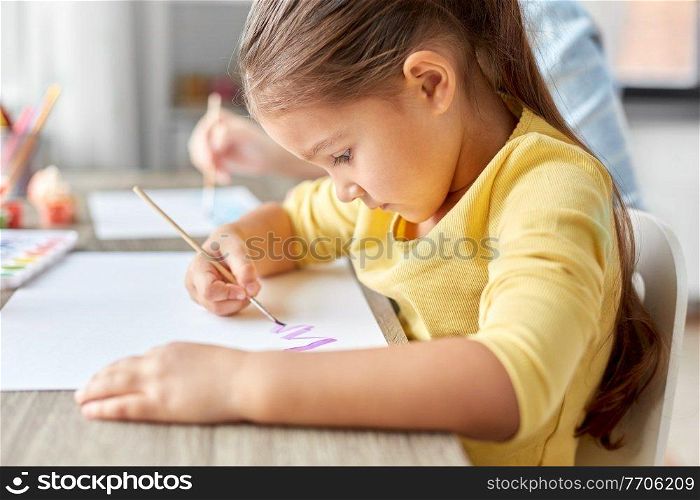 childhood, art and leisure concept - little girl with colors and brush drawing picture on paper at home. little girl drawing picture with colors and brush