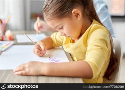 childhood, art and leisure concept - little girl with colors and brush drawing picture on paper at home. little girl drawing picture with colors and brush