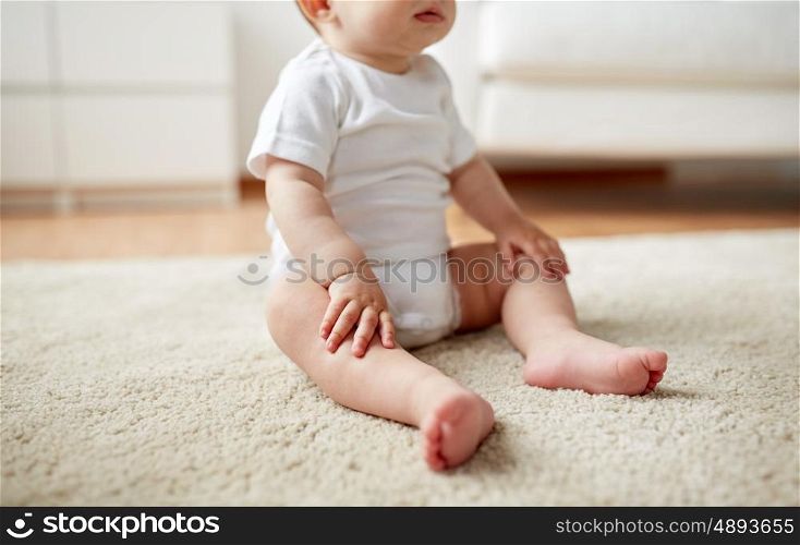 childhood, babyhood and people concept - happy little baby boy or girl sitting on floor at home