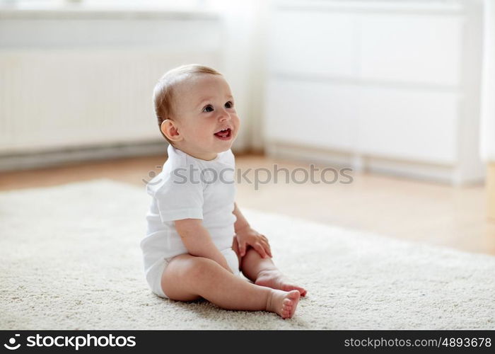 childhood, babyhood and people concept - happy little baby boy or girl sitting on floor at home