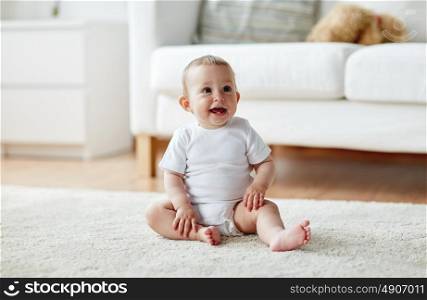 childhood, babyhood and people concept - happy little baby boy or girl sitting on floor at home. happy baby boy or girl sitting on floor at home