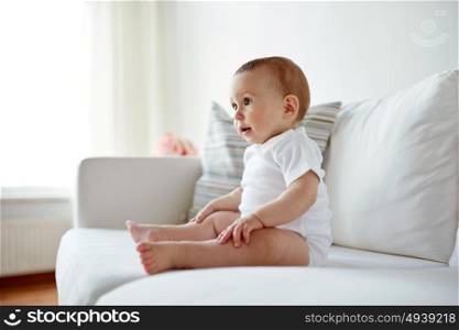 childhood, babyhood and people concept - happy little baby boy or girl sitting on sofa at home. happy baby boy or girl sitting on sofa at home