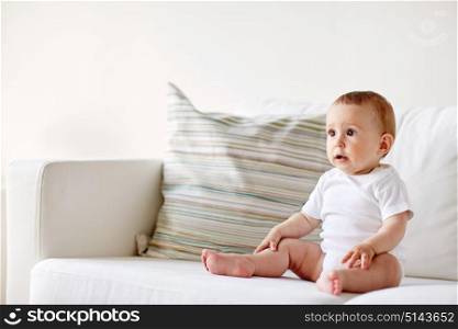childhood, babyhood and people concept - happy little baby boy or girl sitting on sofa at home. happy baby boy or girl sitting on sofa at home