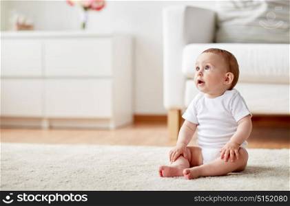 childhood, babyhood and people concept - happy little baby boy or girl sitting on floor at home. happy baby boy or girl sitting on floor at home