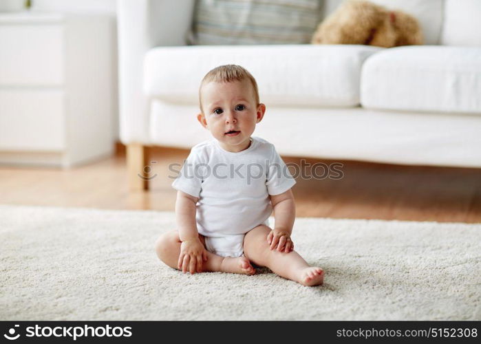 childhood, babyhood and people concept - happy little baby boy or girl sitting on floor at home. happy baby boy or girl sitting on floor at home