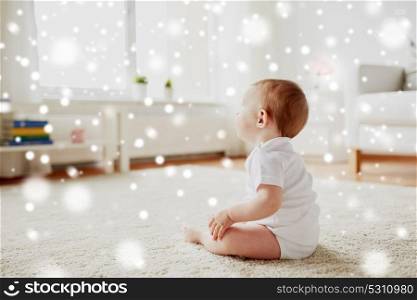 childhood, babyhood and people concept - happy little baby boy or girl sitting on floor at home over snow. happy baby boy or girl sitting on floor at home