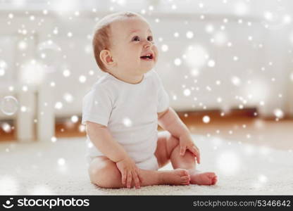 childhood, babyhood and people concept - happy little baby boy or girl sitting on floor with soap bubbles around at home over snow. happy baby with soap bubbles at home