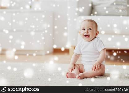 childhood, babyhood and people concept - happy little baby boy or girl sitting on floor at home over snow. happy baby boy or girl sitting on floor at home