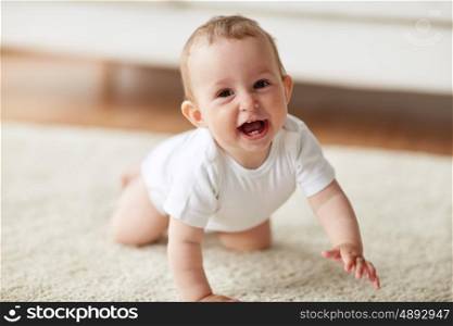 childhood, babyhood and people concept - happy smiling little baby boy or girl crawling on floor at home