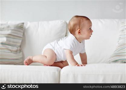 childhood, babyhood and people concept - little baby boy or girl crawling along sofa at home