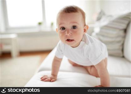 childhood, babyhood and people concept - little baby boy or girl crawling along sofa at home. little baby in diaper crawling along sofa at home
