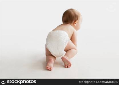 childhood, babyhood and people concept - little baby boy or girl in diaper crawling on white floor