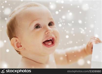 childhood, babyhood, emotions and people concept - face of happy little baby boy or girl looking up and holding to table over snow. face of happy little baby boy or girl looking up