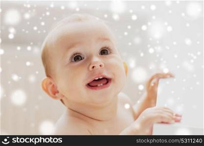 childhood, babyhood, emotions and people concept - face of happy little baby boy or girl looking up and holding to table over snow. face of happy little baby boy or girl looking up