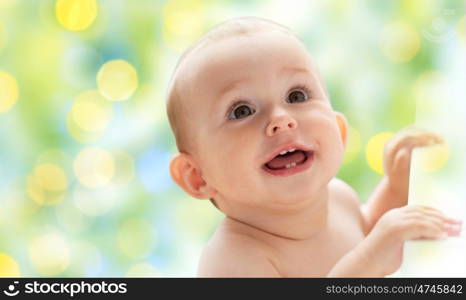 childhood, babyhood, emotions and people concept - happy little baby boy or girl looking up over green holidays lights background