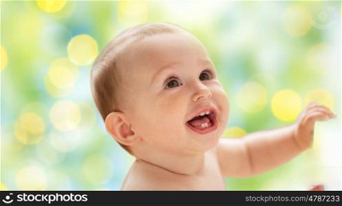 childhood, babyhood, emotions and people concept - happy little baby boy or girl looking up over green holidays lights background