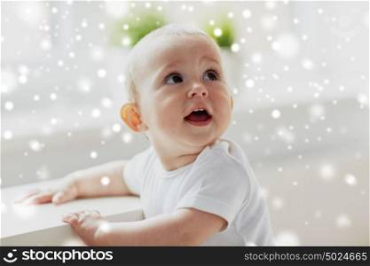 childhood, babyhood, emotions and people concept - happy little baby boy or girl holding to table over snow. happy little baby boy or girl holding to table