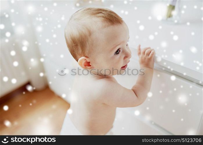 childhood, babyhood, emotions and people concept - happy little baby boy or girl holding to table over snow. happy little baby boy or girl holding to table