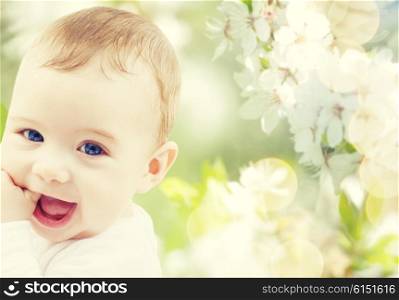 childhood, babyhood, summer, spring and health concept - closeup of happy baby boy or girl over green blooming garden background