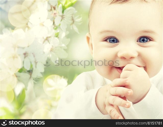 childhood, babyhood, summer, spring and health concept - closeup of happy baby boy or girl over green blooming garden background