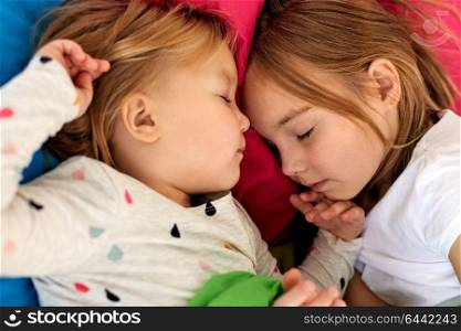 childhood, bedtime and family concept - happy little girls or sisters sleeping in bed at home. happy little girls sleeping in bed at home