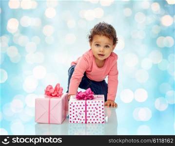childhood, birthday, holidays and people concept - little african american baby girl with gift boxes and confetti crawling on floor over blue holidays lights background
