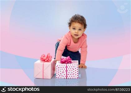 childhood, birthday, holidays and people concept - little african american baby girl with gift boxes and confetti crawling on floor over pink and violet background