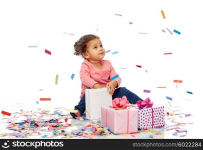 childhood, birthday, party, holidays and people concept - happy little african american baby girl with gift boxes and confetti playing with shopping bag sitting on floor