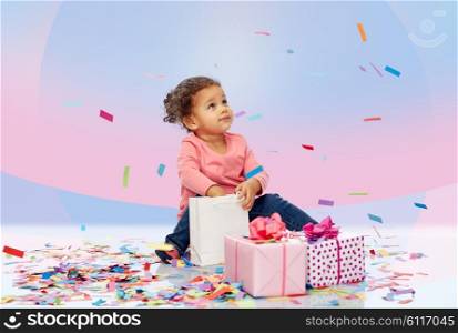 childhood, birthday, party, holidays and people concept - happy little african american baby girl with gift boxes and confetti playing with shopping bag sitting on floor over pink violet background