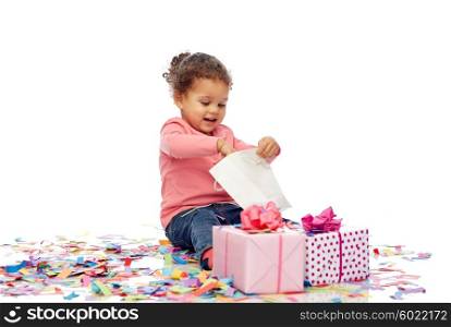 childhood, birthday, party, holidays and people concept - happy smiling little african american baby girl with gift boxes and confetti playing with shopping bag and sitting on floor